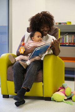 Mother reading a book to her baby daughter in a library