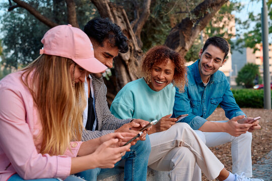Friends engaged in lively conversation while using phones in a park