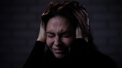 Silhouette of woman with mental health issues, sitting on the sofa, depressed expression, covering ears with hands, holding head, close shot.