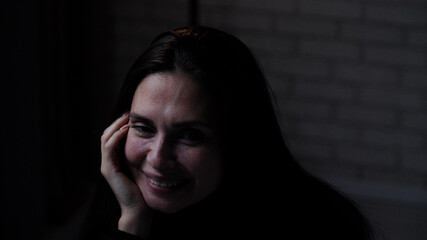 Silhouette of woman suffering mental health issues, sitting at the table in front of camera, depressed expression, thinking, bitter smiling tired face, close up.