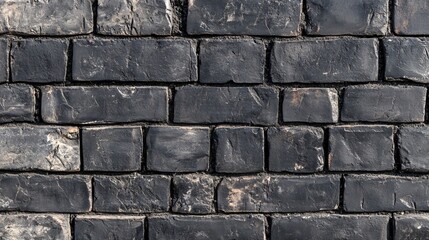 Fototapeta premium Close-up of a textured black stone wall with uneven bricks, creating an industrial and rustic ambiance.