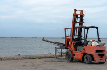 A red forklift sits on a concrete platform on the side of the road by the water's edge