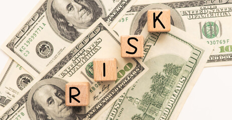 Word "RISK" in wooden block on US Dollar bills