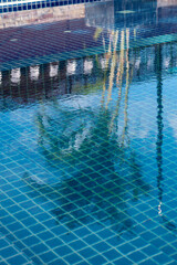 Surface of a swimming pool with reflects the patterns of blue tiles  and palm trees
