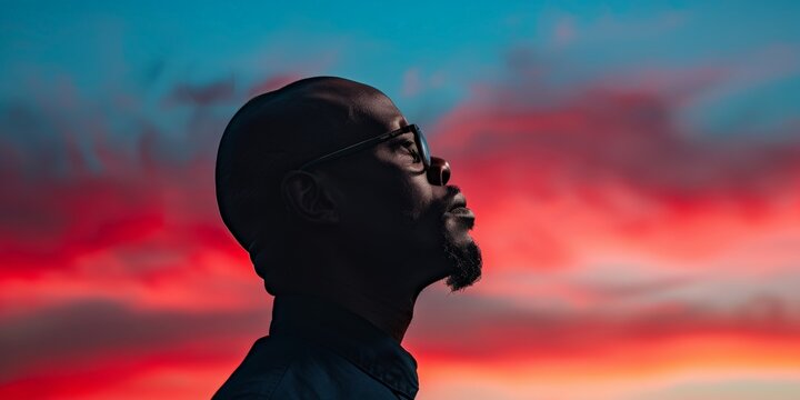 Silhouette of a bearded man gazing upward at a colorful sunset sky, evoking feelings of introspection and wonder. - Powered by Adobe