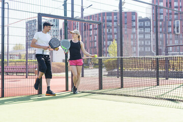 Sports couple with padel rackets posing on tennis court