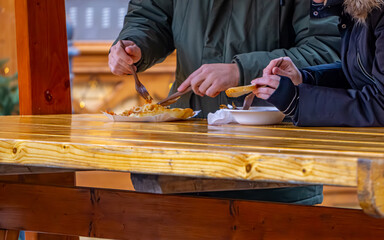 people eating cabbage with peas, fish and other Christmas foods at the Christmas market in the city. people eating at wooden tables.
