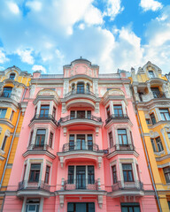 Fototapeta premium Pink and yellow apartment building with decorative balconies and ornate details stands tall against a cloudy blue sky