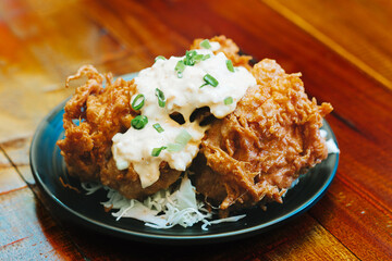 Crispy fried chicken karaage with creamy sauce on a plate on a wooden table. Japanese cooking technique that involves deep-frying small pieces of meat or fish in oil.