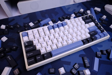 Fototapeta premium Modern 75% Layout White Mechanical Keyboard With Minimalist Theme of White, Blue, and Black Keycaps on a Blue Deskmat, with Scattered Keycaps