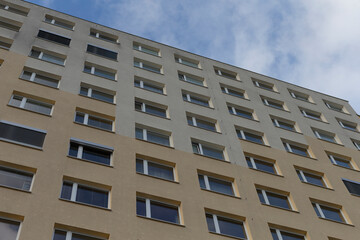 A residential building facade featuring numerous windows set against a backdrop of a cloudy sky