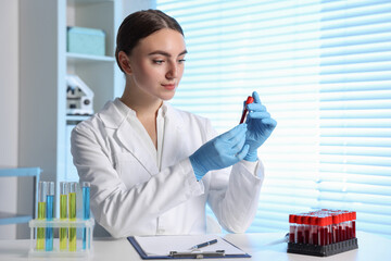Laboratory testing. Doctor holding test tube with blood sample at table indoors