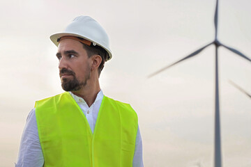 Man engineer wearing safety vest and helmet inspecting wind turbines for renewable energy generation