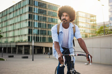 Young African American man with afro hairstyle riding bicycle in urban city