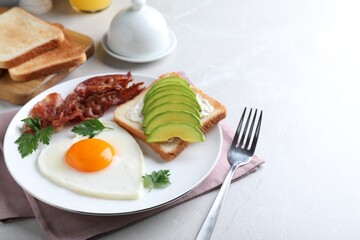 Romantic breakfast with fried bacon, heart shaped egg and avocado toast on light grey table. Valentine's day celebration