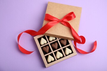 Tasty heart shaped chocolate candies on violet background, flat lay. Happy Valentine's day
