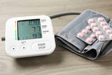 Blood pressure measuring device and pills on wooden table, closeup