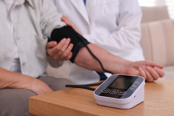 Doctor measuring patient's blood pressure at wooden table indoors, closeup