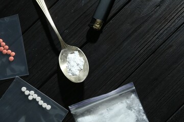 Drug addiction. Plastic bag with powder, spoon cigarette lighter and pills on black wooden table,...