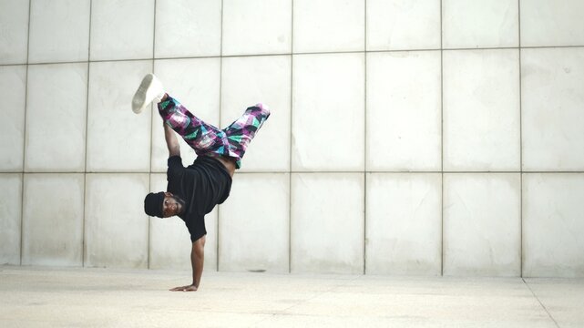 Breakdancer doing a handstand with legs spread in front of white wall