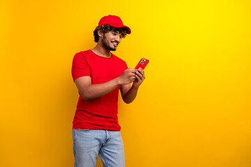 Trendy young man in casual red attire holding smartphone against vibrant yellow background, engaging in work or leisure