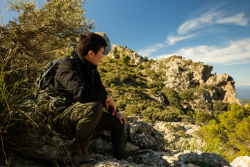 Young hiker sitting on a rock watching the mountains and the panorama from above on a sunny day