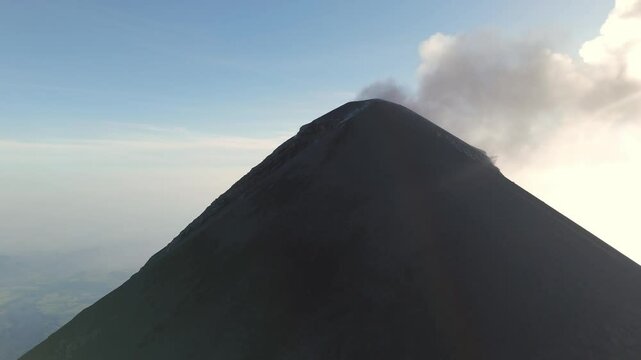 The Fuego Volcano with smoke rising from its summit in the glow of the sunset. A stunning view of this iconic Guatemalan volcano.
