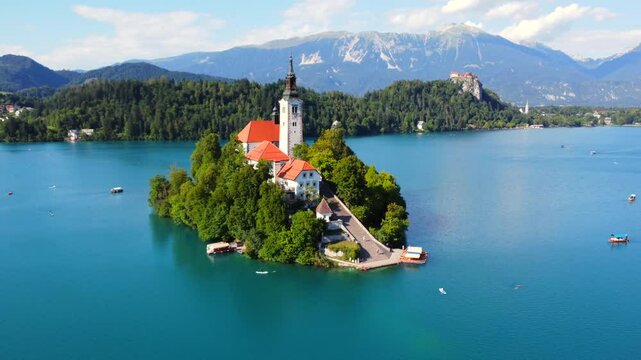 Aerial view of lake bled island with pilgrimage church of the assumption of maria on a sunny summer day with julian alps and bled castle in the background