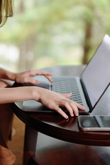 Young woman working on a laptop at a wooden table in a serene natural setting, showcasing productivity and focus in a calm environment