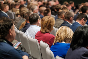 People sitting in chairs at a conference, attentively listening to speakers and presentations.