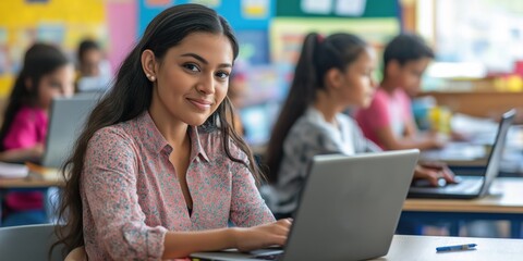 A woman is sitting at a desk with a laptop in front of her. She is smiling and she is enjoying herself. The scene takes place in a classroom setting, with several other people in the background