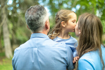 Fototapeta premium Daughter kissing mother while father is holding her in a park