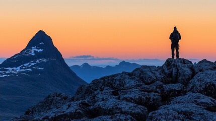 Obraz premium Silhouette of hiker on mountain peak at sunrise, overlooking scenic valley and distant mountains.