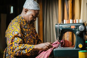 African adult male tailor sewing colorful fabric on vintage sewing machine