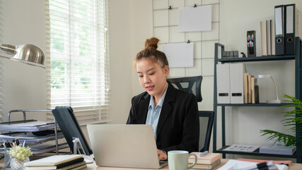 Fototapeta premium Businesswoman sitting at desk on couch in workplace or at home working on laptop and analyzing data on charts and graphs and writing on papers to make business plan and strategies for company, 