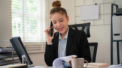 Businesswoman sitting at desk on couch in workplace or at home working on laptop and analyzing data on charts and graphs and writing on papers to make business plan and strategies for company, 