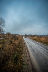 Beautiful road in the field and forest,autumn landscape in woodlands.Mystery and rainy weather with blue and grey sky, forest nature after the rain, road to the forest , water on the road.Wild nature 