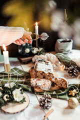 Woman dusting stollen with powdered sugar on a festive table, Scandinavian style, Scandinavian Christmas, stollen with powdered sugar, raisins, candied fruits
