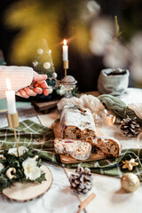 Woman dusting stollen with powdered sugar on a festive table, Scandinavian style, Scandinavian Christmas, stollen with powdered sugar, raisins, candied fruits