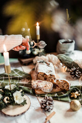 Woman dusting stollen with powdered sugar on a festive table, Scandinavian style, Scandinavian Christmas, stollen with powdered sugar, raisins, candied fruits