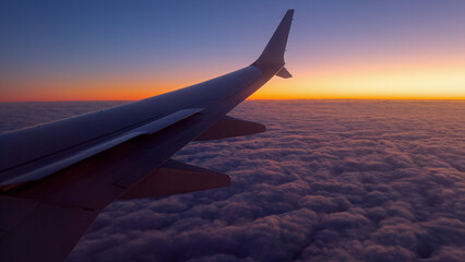 Fototapeta premium Airplane Wing Above Clouds During Vibrant Sunset at High Altitude