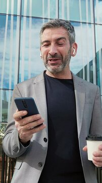 Cheerful businessman using smartphone and drinking coffee