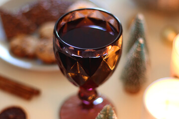 Various Christmas decorations, cookies, chocolate, nuts and tangerines, wine glasses and lit candles on the table. Holiday hygge at home. Selective focus.