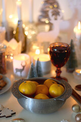 Various Christmas decorations, cookies, chocolate, nuts and tangerines, wine glasses and lit candles on the table. Holiday hygge at home. Selective focus.