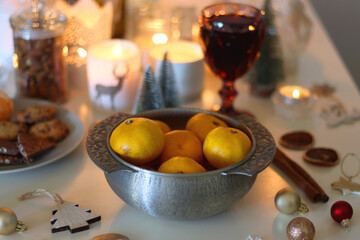 Various Christmas decorations, cookies, chocolate, nuts and tangerines, wine glasses and lit candles on the table. Holiday hygge at home. Selective focus.