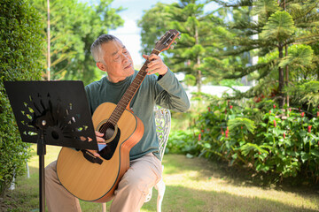 Senior man a veteran guitarist plays music in the garden at home