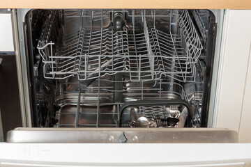 Built-in empty dishwasher with its door open. Modern technologies in the home kitchen with...