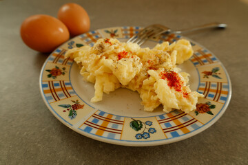 A colorful plate of freshly prepared scrambled eggs seasoned with black pepper and paprika, accompanied by two whole brown eggs on a kitchen countertop.