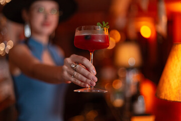 Young beautiful bartender girl made a delicious fresh alcoholic cocktail and gives it to the camera