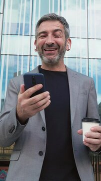 Smiling businessman using smartphone and drinking coffee in slow motion